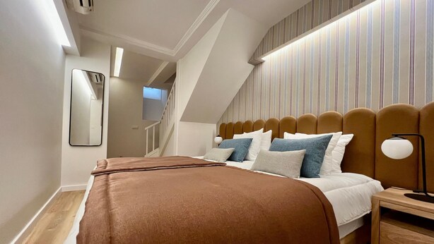 A bedroom with a bed, a nightstand, a lamp, a mirror, and a striped wall. - Santos · Designer Retreat: 1 Bedroom apt (Lisbon)