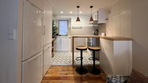 A compact kitchen with white cabinets, a wooden countertop, two stools, and pendant lights. - Santos · Designer Retreat: 1 Bedroom apt (Lisbon)