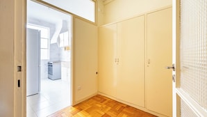 A room with a wooden parquet floor, a white wardrobe, and a door leading to a kitchen area. - Marino · 3bed apt Close to Casa da Musica (Porto)