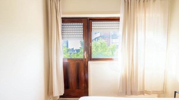 A bedroom with a wooden door, a window with sheer curtains, and a bed with a white duvet. - Marino · 3bed apt Close to Casa da Musica (Porto)