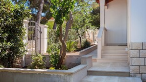 A modern building with a stone facade, a set of concrete steps leading to a covered entrance, and a metal gate. - Impeccable 3-bed House in Supetar (Supetar)