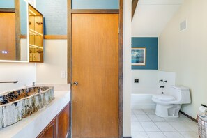 A bathroom with a wooden door, a sink with a unique stone basin, a white toilet, and a framed picture on the wall.