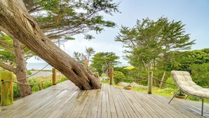 A wooden deck with a lounge chair, surrounded by trees and a view of the sea. - Moss Beach Oceanfront Retreat ~ 20 Mi to San Fran! (Moss Beach)