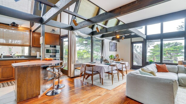 A modern kitchen with a wooden island, dining area with a table and chairs, and a large window with a view of greenery. - Moss Beach Oceanfront Retreat ~ 20 Mi to San Fran! (Moss Beach)