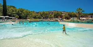 A large outdoor swimming pool with clear water, surrounded by rocks and palm trees.