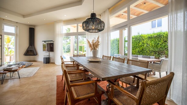 Een ruime eethoek met een lange houten tafel, rieten stoelen en een moderne hanglamp.