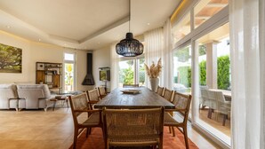 Een ruime eetruimte met een grote houten tafel, rieten stoelen en een hanglamp.