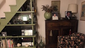A living room with a wooden staircase, a bookshelf, a floral armchair, and a cabinet with a vase and picture frames. - Coquet Appartement Bastia vue sur mer (Bastia)