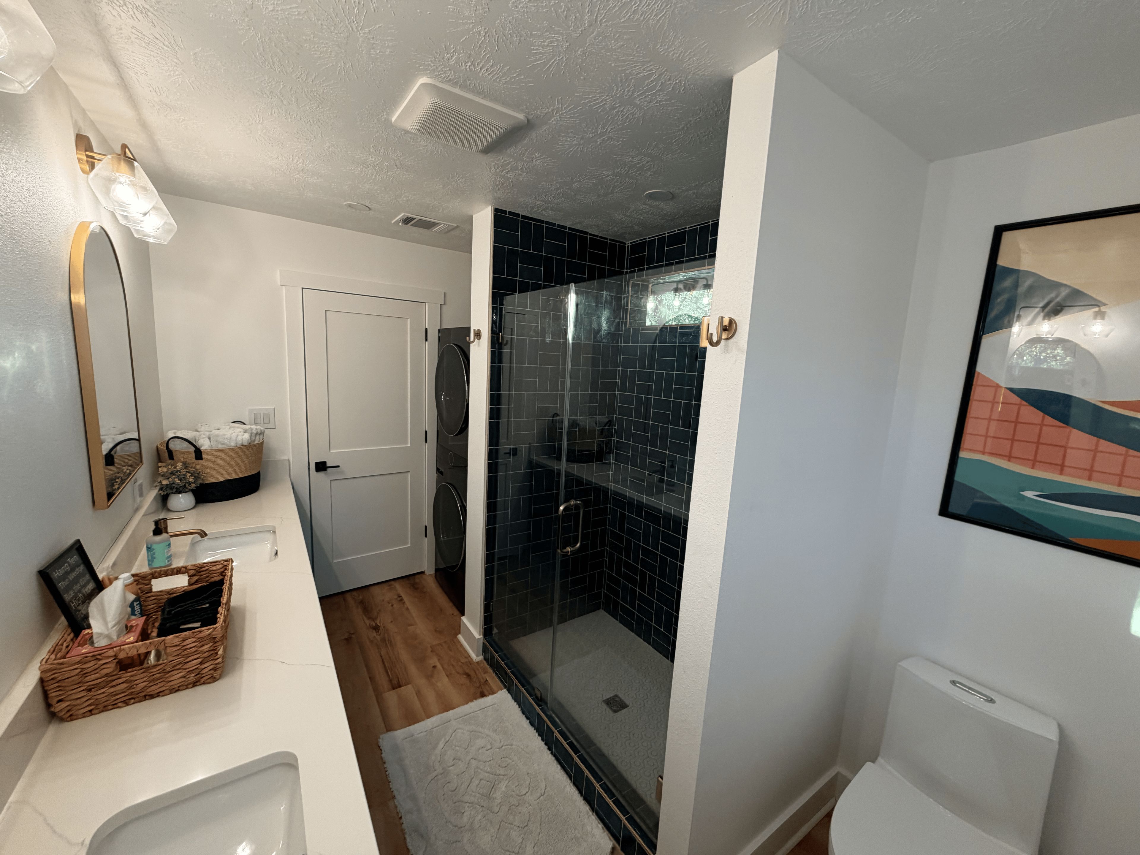 A bathroom with a white sink, a mirror, a shower with black tiles, and a framed picture on the wall.