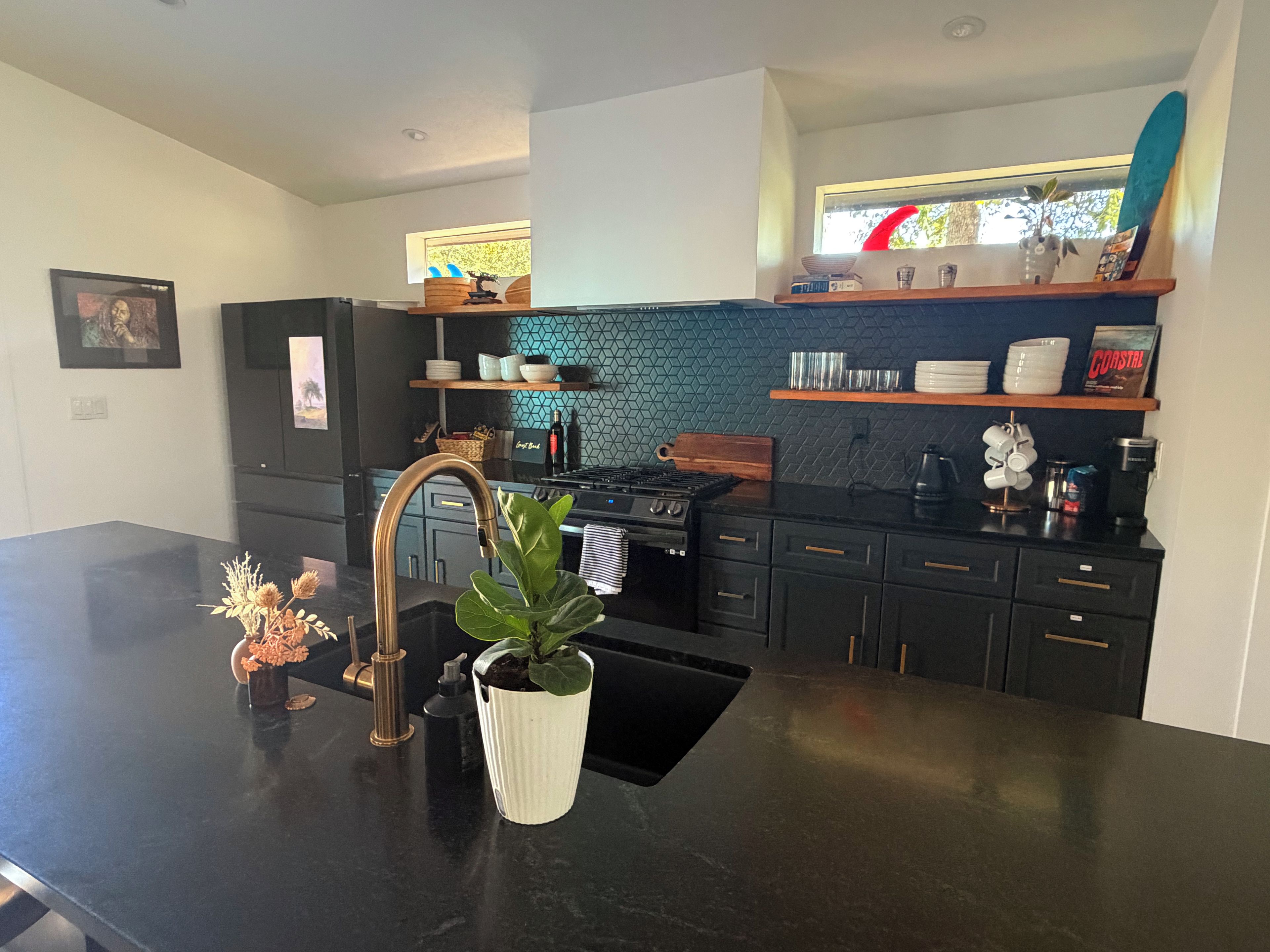 A modern kitchen with a black countertop, stainless steel appliances, and a backsplash with a geometric pattern.
