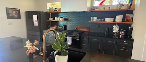 A modern kitchen with a black countertop, stainless steel appliances, and a backsplash with a geometric pattern.
