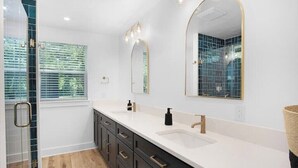 A modern bathroom with a double sink, a large mirror, and a shower area. - Modern Backyard Casita (Bryan)