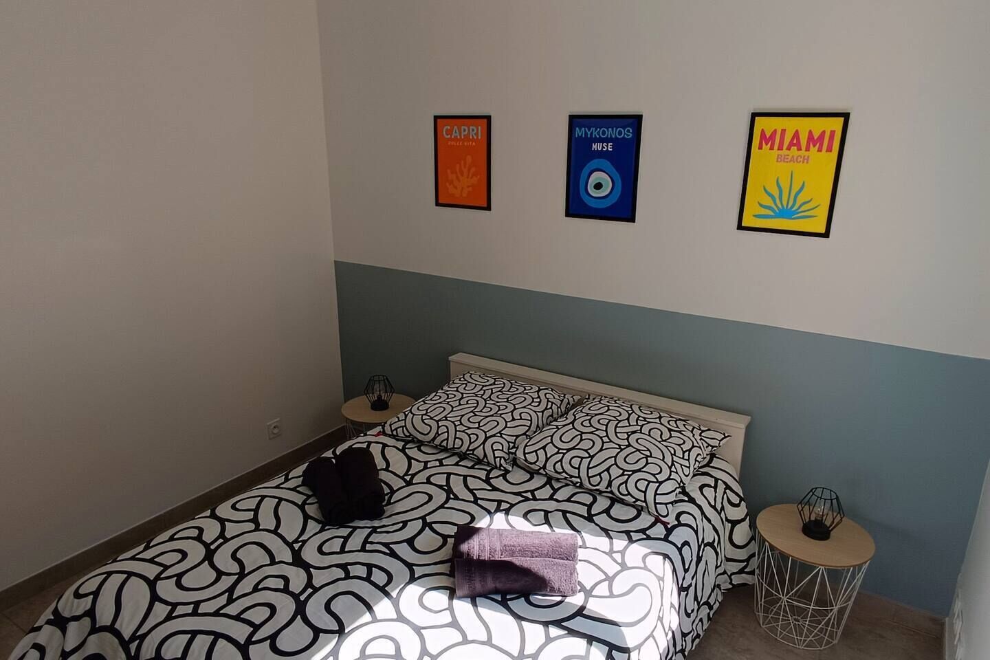 Une chambre à coucher avec un lit, des oreillers, une table de chevet et des œuvres d’art murales.