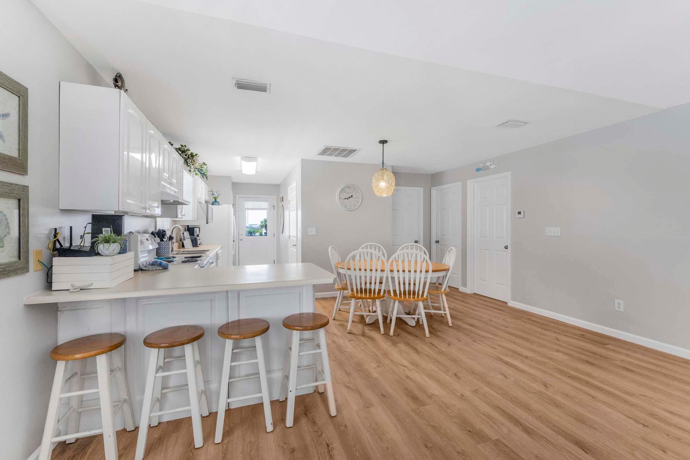 A modern kitchen with white cabinets, a wooden dining table with four chairs, and a bar area with stools.