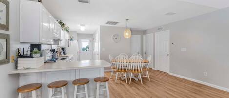 A modern kitchen with white cabinets, a wooden dining table with four chairs, and a bar area with stools.