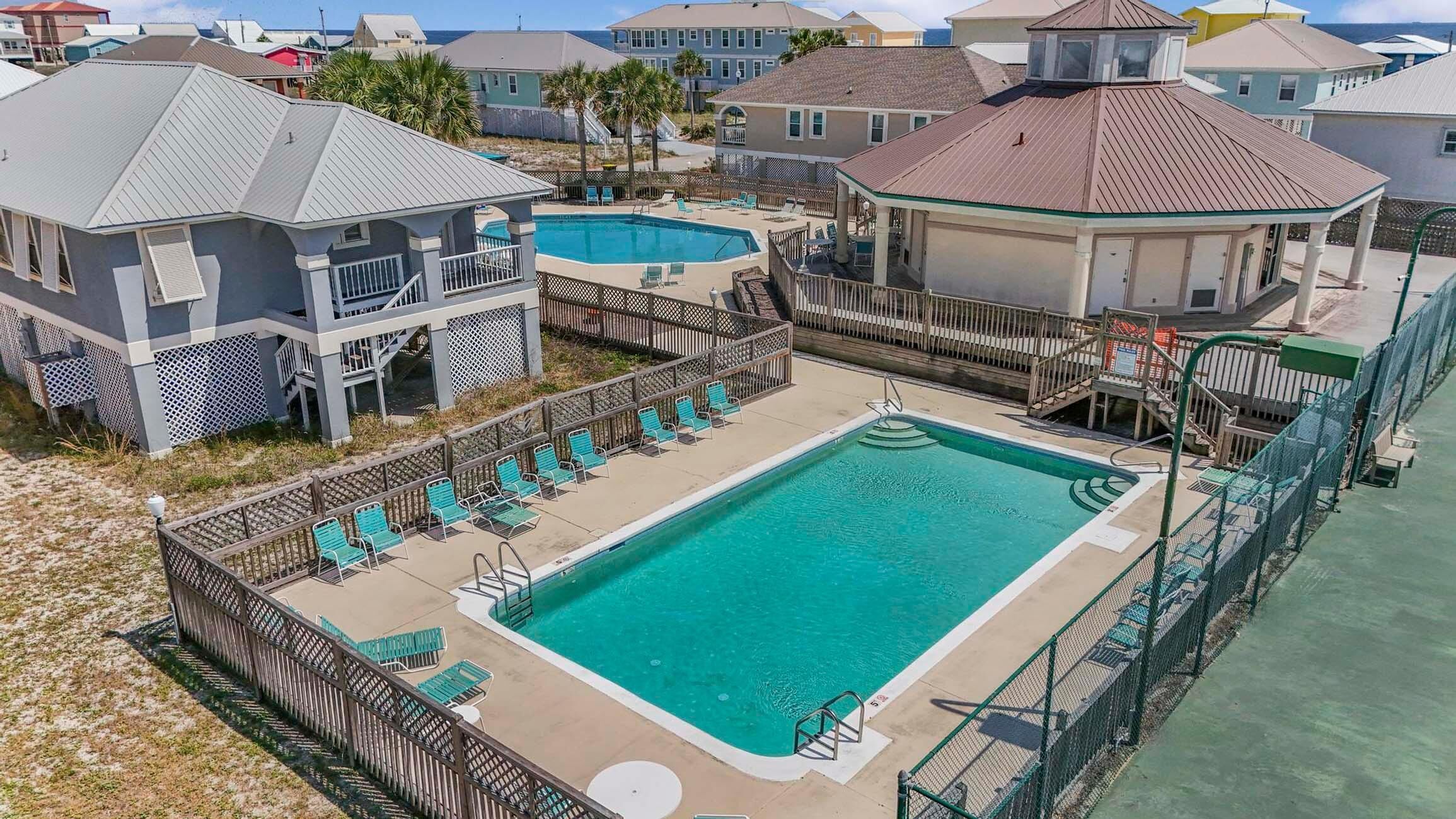 A pool area with a rectangular pool, surrounded by a wooden fence and multiple lounge chairs.