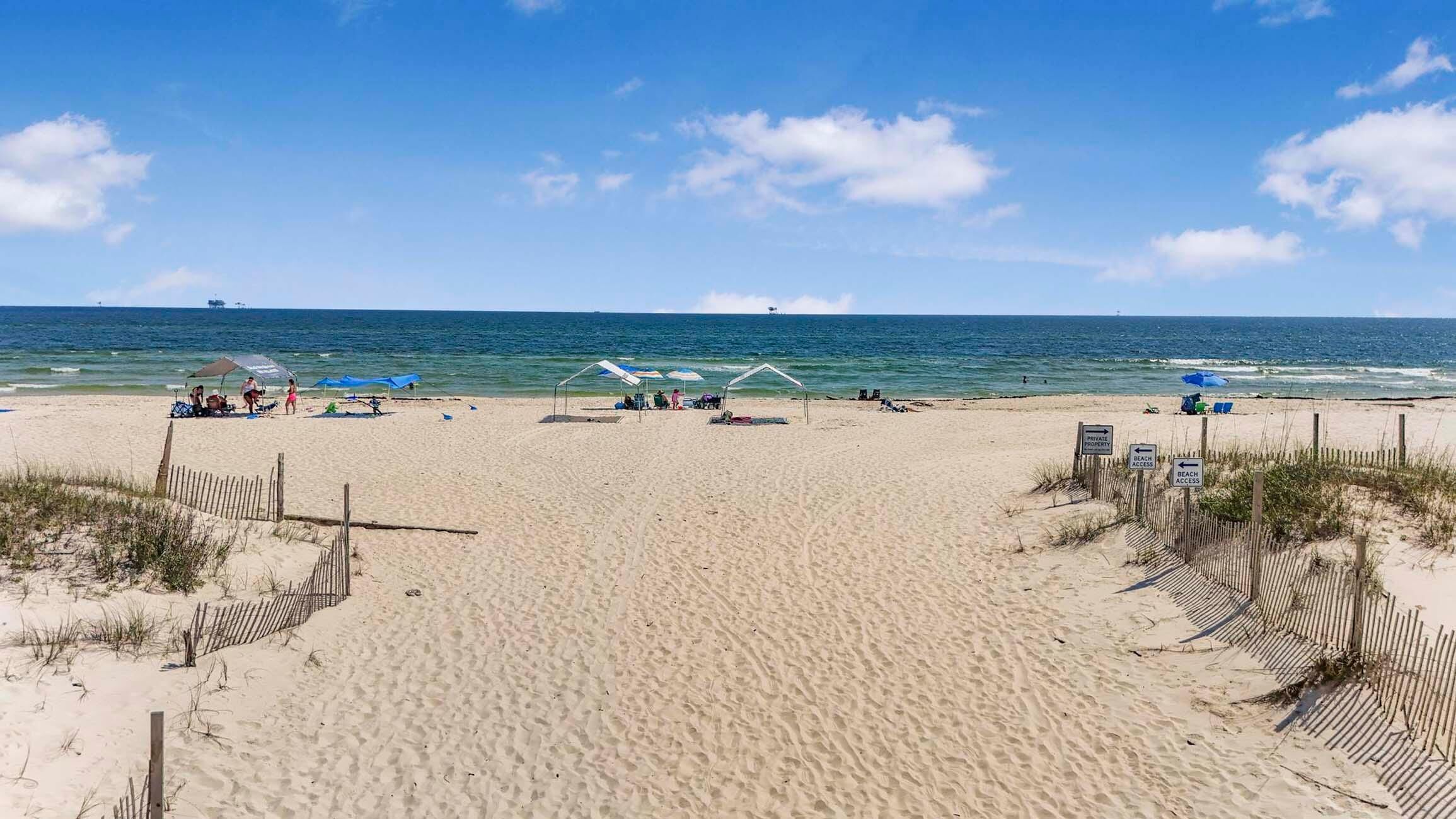 Une plage avec un rivage sablonneux, une clôture en bois et un ciel bleu dégagé.
