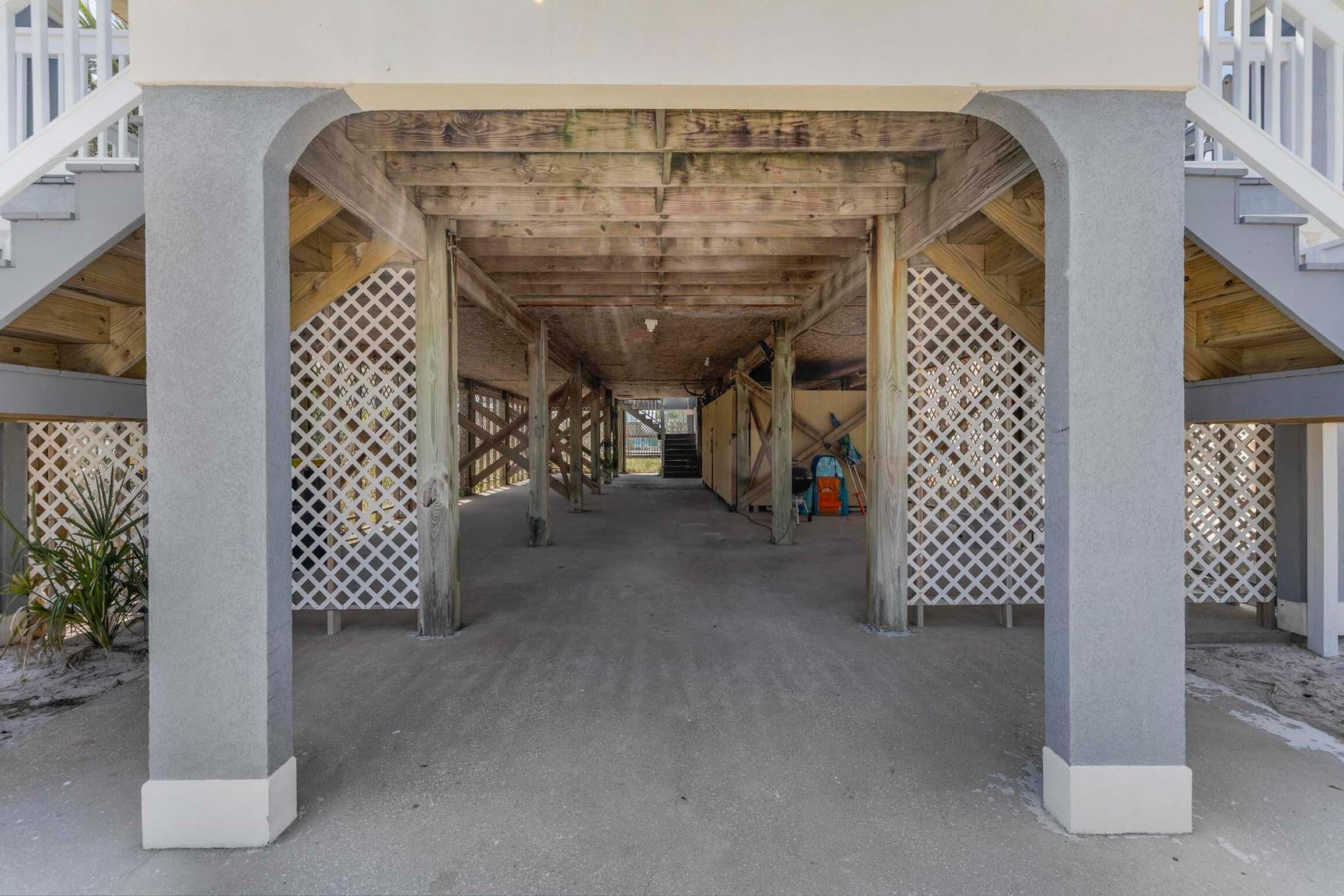 A covered walkway with concrete pillars and wooden beams, leading to a staircase.