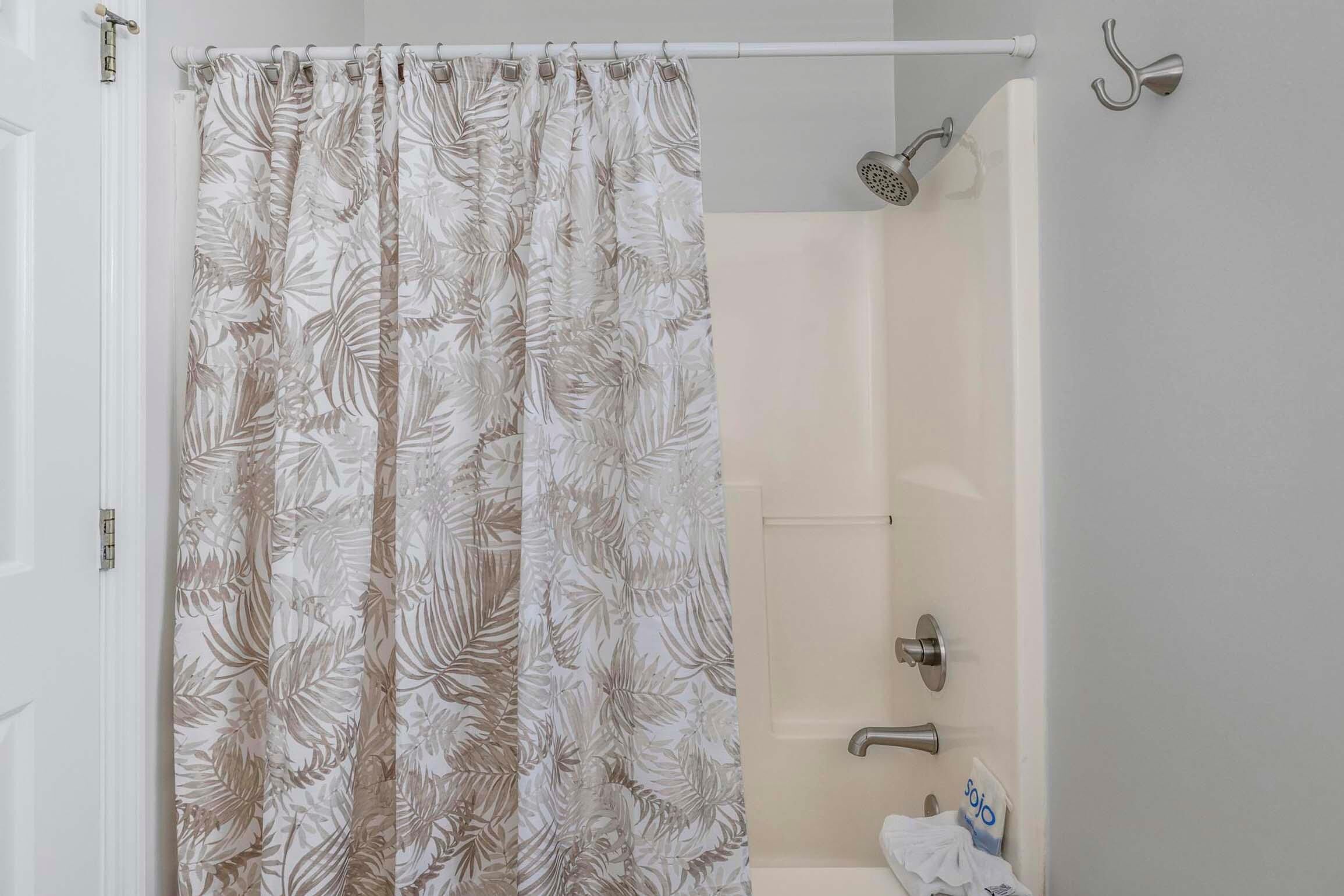 A bathroom with a shower curtain featuring a leaf pattern, a white bathtub, a towel rack, and a showerhead.