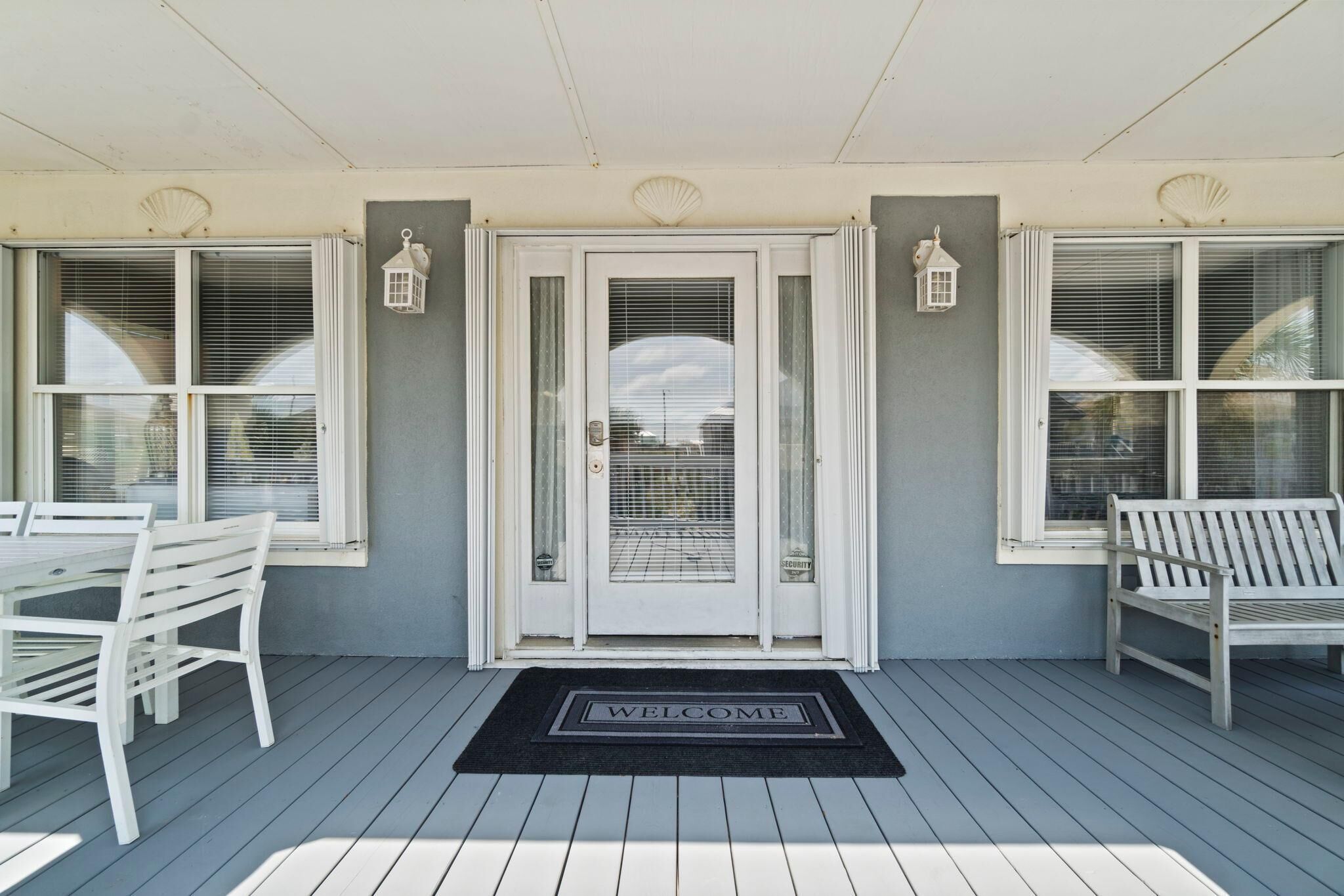 A covered porch with a white door, two white benches, and a welcome mat.