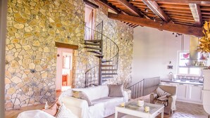 A stone-walled living area with a spiral staircase, white furniture, and a kitchen in the background. - Villa surrounded by vineyards with private pool near Orvieto (Terni)