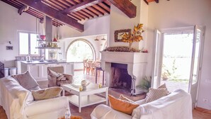 A spacious living room with white furniture, a fireplace, and a kitchen in the background. - Villa surrounded by vineyards with private pool near Orvieto (Terni)