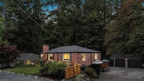 A brick house with a garage, surrounded by trees and a gravel driveway. - Hidden Forest Retreat | King | Firepit | Near Light Rail | Minutes to Downtown Seattle (Seattle)