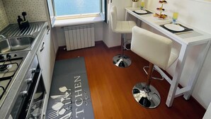 A compact kitchen with a view of a lake, a dining area with a white table and chairs, and a kitchen island with a 'KITCHEN' mat. - Rooftop cannobio (San Bartolomeo)