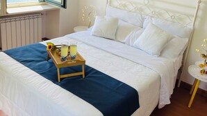 A neatly made bed with white linens and a blue accent, a wooden tray with a glass of juice and a flower, and a painting of a night scene on the wall. - Rooftop cannobio (San Bartolomeo)
