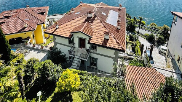 A residential area with terracotta-tiled roofs, a clear blue sky, and a lake with mountains in the background. - Rooftop cannobio (San Bartolomeo)