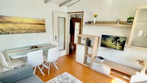 A modern living room with a sofa, a dining area with a table and chairs, a TV, and a painting on the wall. - Rooftop cannobio (San Bartolomeo)