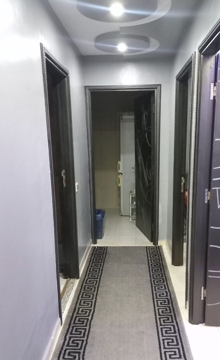 A hallway with a patterned rug, a ceiling light, and a door leading to a room with a washing machine.