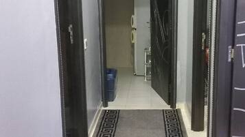 A hallway with a patterned rug, a ceiling light, and a door leading to a room with a washing machine.