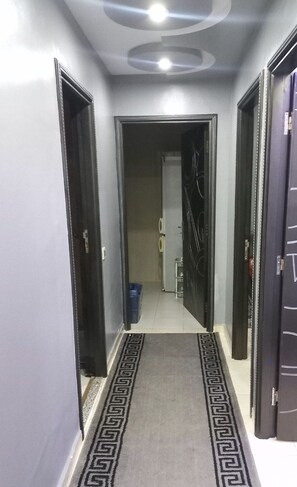 Un couloir avec un tapis à motifs, des portes de part et d’autre, et un luminaire au plafond.