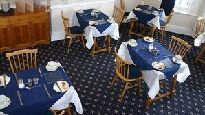 A dining area with multiple tables and chairs, each set with plates, cutlery, and glasses. - Sefton Lodge  (Paignton)