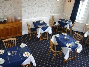 A dining area with multiple tables and chairs, each set with plates, cutlery, and glasses. - Sefton Lodge  (Paignton)