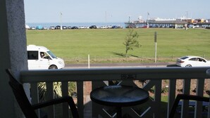 A balcony with a view of a grassy field and parked cars. - Sefton Lodge  (Paignton)