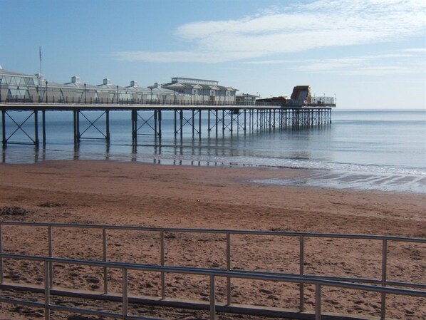 A beach with a pier extending into the water, featuring buildings and a lifeguard tower. - Sefton Lodge (Paignton)