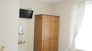 Una habitación con un armario de madera, un televisor montado en la pared y una ventana con cortinas.