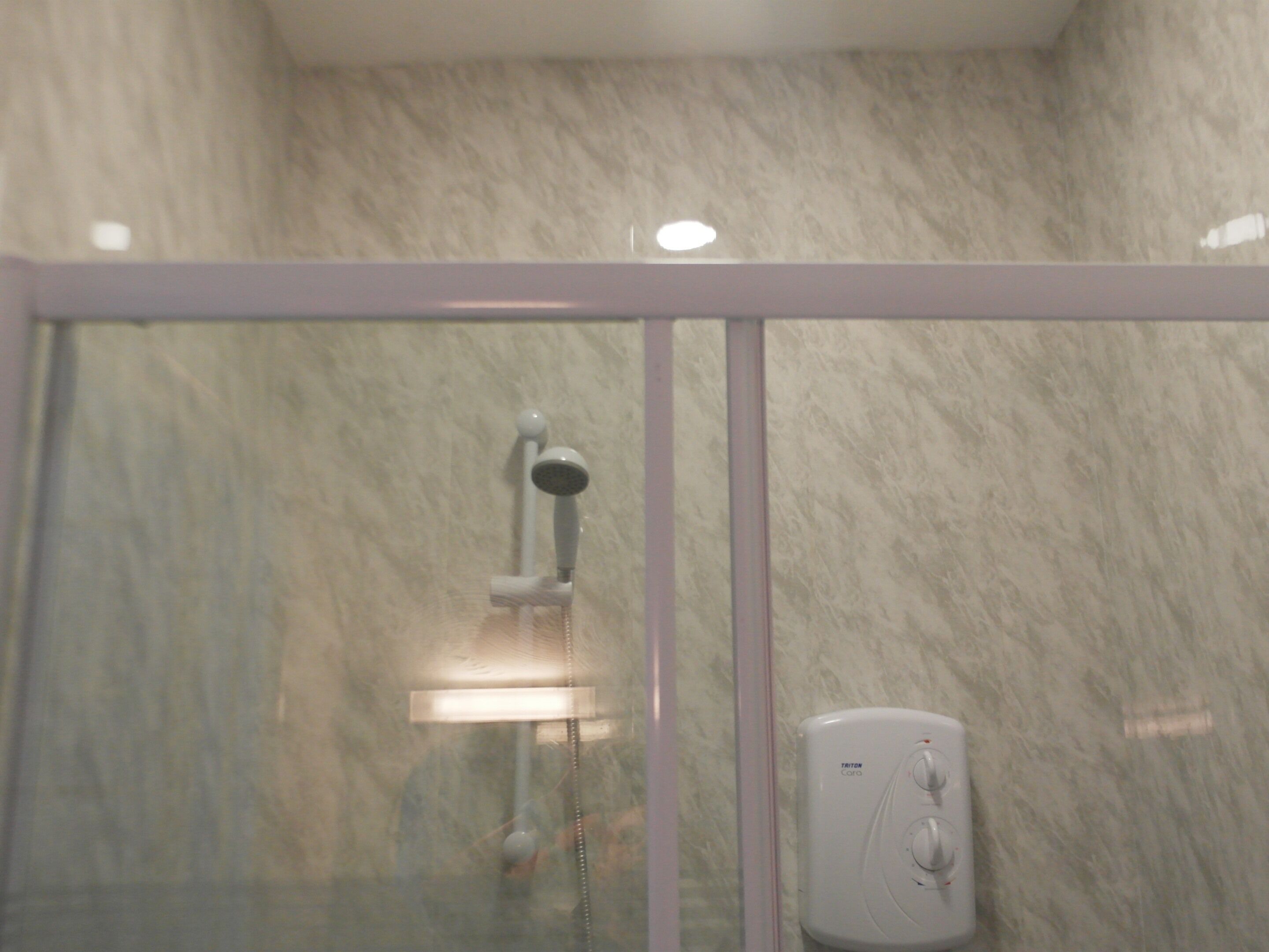 Een badkamer met een douchecabine van glas, een handdouche en een bedieningspaneel aan de muur.
