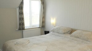 Una cama bien hecha con estampado floral, una ventana con cortinas y una lámpara fijada a la pared.