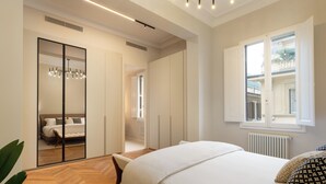 Une chambre moderne avec un grand lit, un dressing et une fenêtre donnant sur la ville.