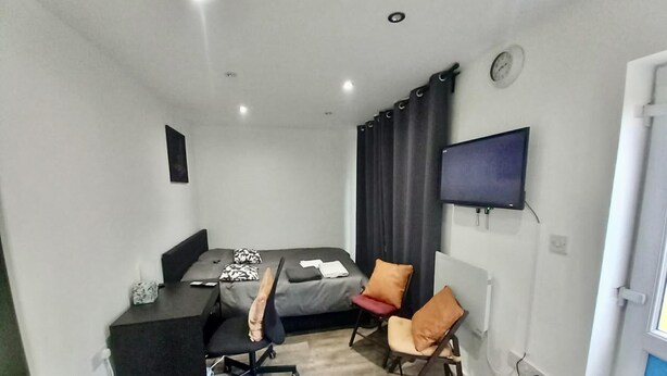 Ein kleines Zimmer mit einem Bett, einem Schreibtisch, einem Stuhl, einem Fernseher und einem Mülleimer.