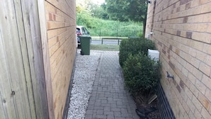 Ein schmaler Ziegelweg führt zu einem ehrverzierten Eingang, begleitet von einem Holzzaun auf der einen Seite und einem Metallzaun auf der anderen.