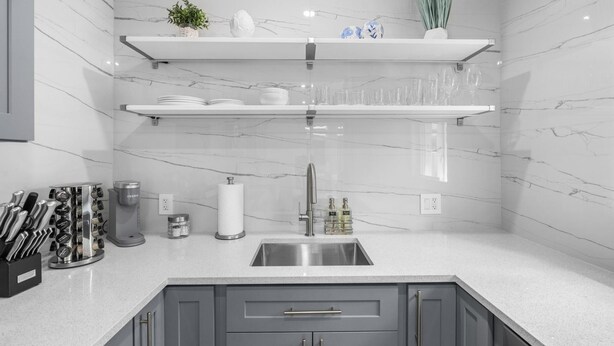 Una cocina moderna con gabinetes grises, un lavamanos de acero inoxidable y salpicadero de mármol blanco.