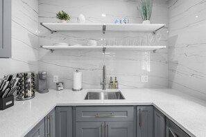 A modern kitchen with grey cabinets, a stainless steel sink, and white marble backsplash. - Uhost AI 1BR With Marble Accents Patio (Fort Lauderdale)