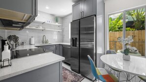 Una cocina moderna con refrigerador de acero inoxidable, armarios blancos y una zona de comedor con mesa redonda y sillas coloridas.