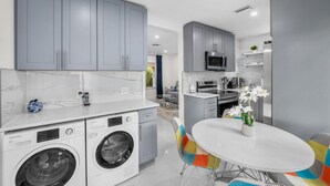 Una cocina moderna con armarios grises, un microondas integrado y un comedor con mesa blanca y sillas coloridas.