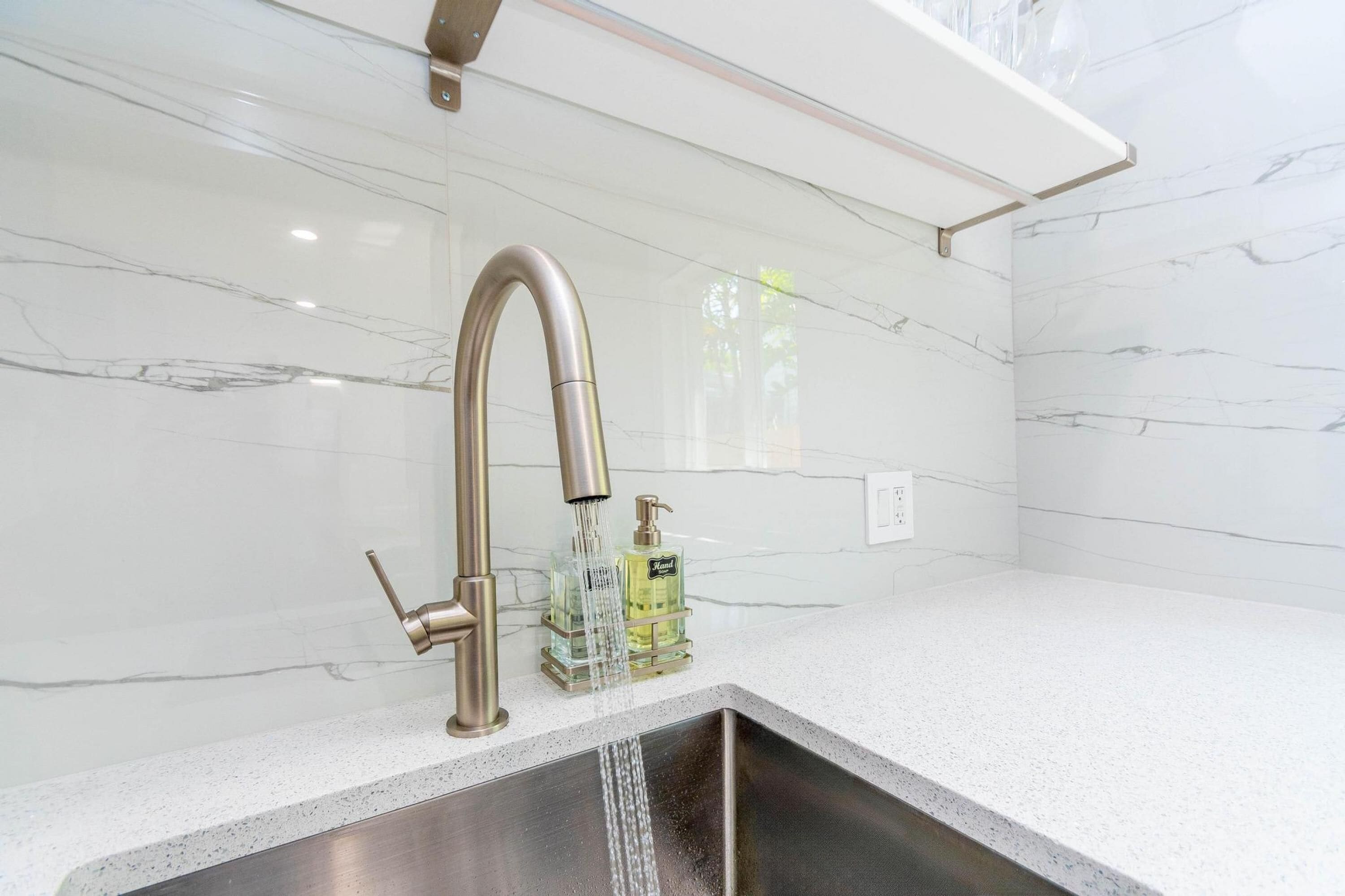 A modern bathroom with a stainless steel sink, a marble backsplash, and a handheld showerhead.