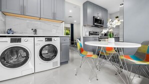 Una cocina moderna con armarios grises, lavadora integrada, microondas y un comedor con sillas de colores.
